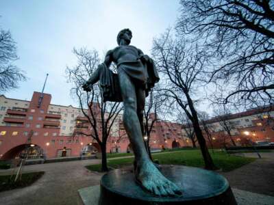 A statue is displayed in front of Karl-Marx-Hof, a red, several-story tall community owned apartment building in Vienna.