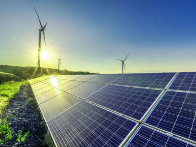 Wind turbines are seen on the horizon as solar panels lay across the grass in the foreground