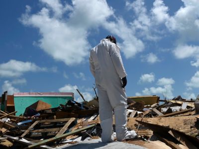 A man in a white HAZMAT suit stands on top of rubble