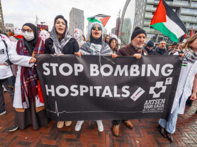 Medical professionals wearing Keffiyehs over their work uniforms march behind a banner reading: "STOP BOMBING HOSPITALS" during an outdoor protest