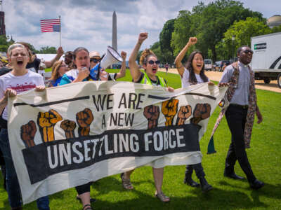 People march behind a banner reading "WE ARE A NEW UNSETTLING FORCE" during an outdoor rally