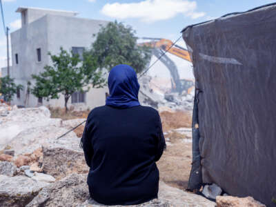 A woman in a blue hijab watches Israeli forces tear down her home