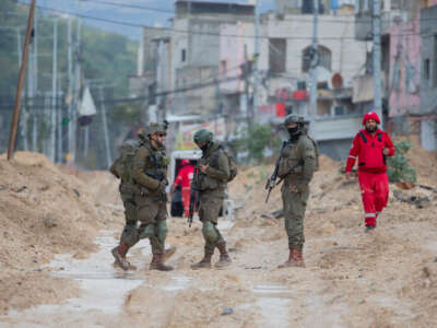 Israeli soldiers walk along a muddy street as a humanitarian worker walks by in Nur Shams refugee camp in the West Bank, Palestine, on February 10, 2025.