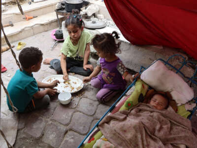 Palestinian children share a meal of rice as a baby sleeps, inside a tent at a displacement camp near Gaza City's port on May 22, 2025.