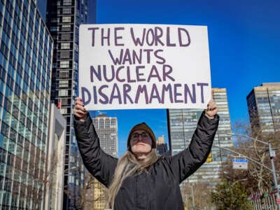 A person holds a sign reading "THE WORLD WANTS NUCLEAR DISARMAMENT" during an outdoor protest