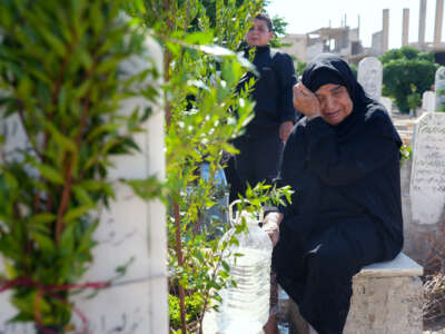 A woman weeps at a grave site as people around her plant olive trees