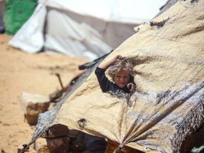 A little girl stands up through a hole in the tent that she and her family lives in
