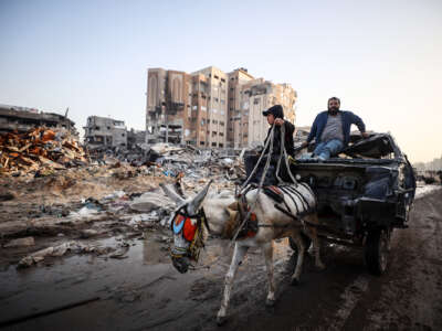 A donkey pulls a cart carrying a man through the rubble that was once a neighborhood