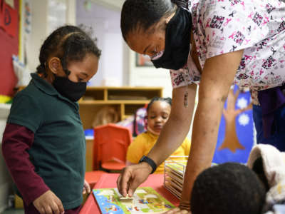 Shanikia Johnson, a teacher, helps a three-year-old clean up a puzzle at Little Flowers Early Childhood and Development Center in the Sandtown-Winchester neighborhood of Baltimore, Maryland, on January 12, 2021.