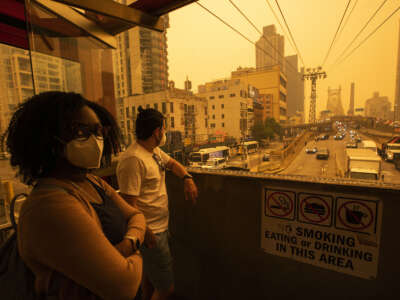 People wear masks as they wait for the tramway to Roosevelt Island as smoke from Canadian wildfires casts a haze over the area on June 7, 2023, in New York City.