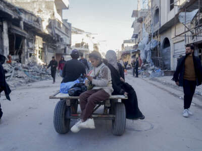 A young girl checks her smartphone on the back of a cart as in Northern Gaza, on February 28, 2025.