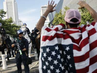 A protester wearing an American flag holds up his hands in front of police amid protests in Los Angeles, California, on June 14, 2025.