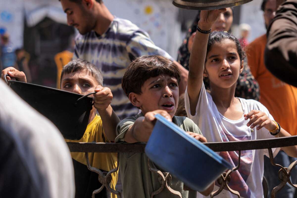 Children queue with pots to receive meals from a charity kitchen in Gaza City on July 14, 2025.
