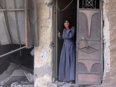 A Palestinian woman standing in a doorway observes the aftermath of an Israeli strike that hit Gaza City's southern Al-Zaytoun neighborhood on August 8, 2025.