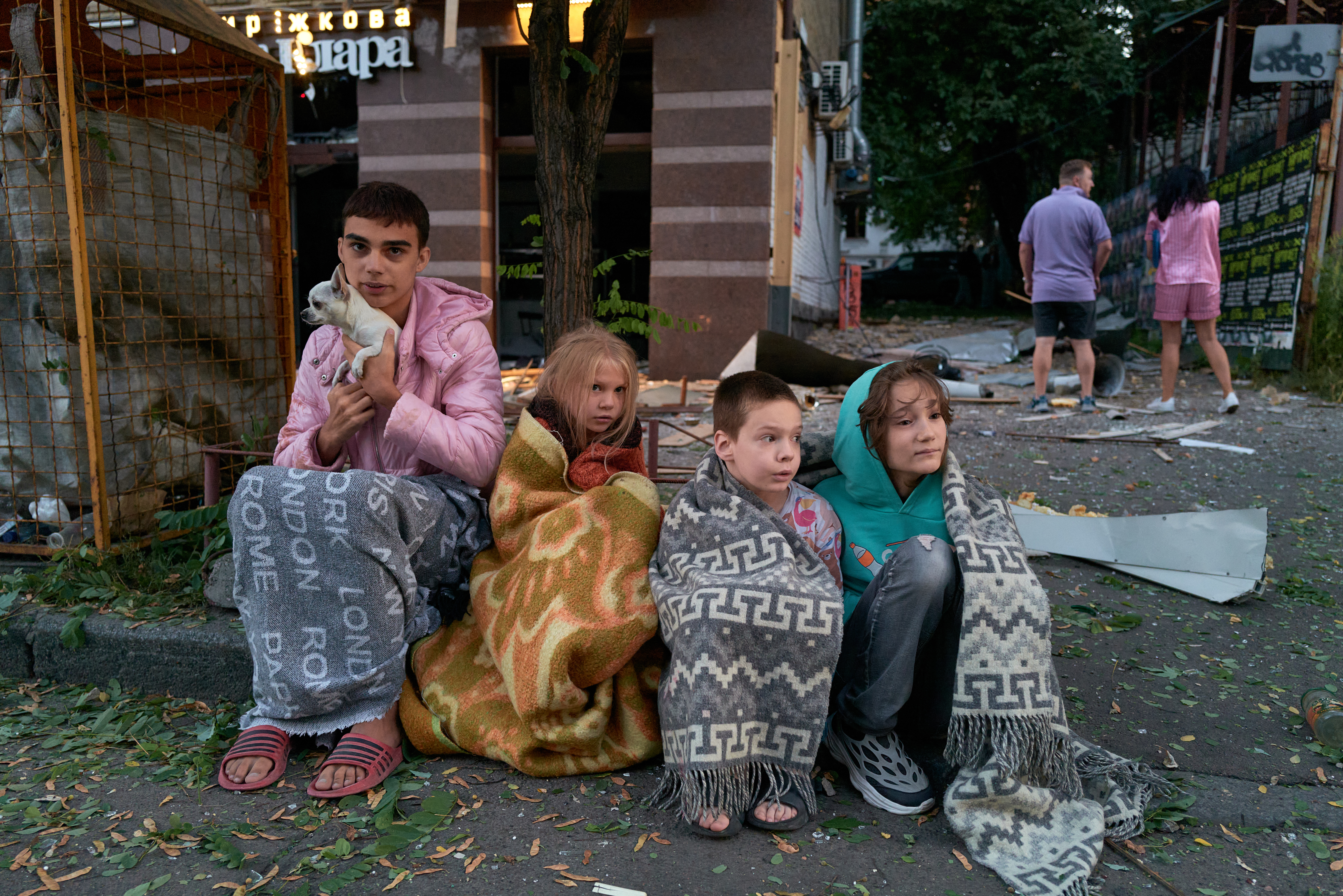 Children sit on the pavement outside a residential building after a Russian ballistic missile struck a bank building in the city center on August 28, 2025, in Kyiv, Ukraine.