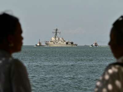 People watch the USS Gravely, a U.S. Navy warship, departing the Port of Spain on October 30, 2025. The warship arrived in Trinidad and Tobago on October 26, 2025, for joint exercises near the coast of Venezuela.