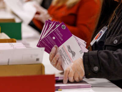 A person with transparent gloved is holding a stack of mail-in ballots.