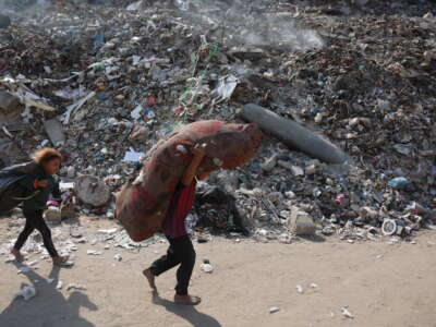 Palestinian children carry their belongings past an unexploded missile in a rubbish dump at the Firas market area of Gaza City, on November 12, 2025.