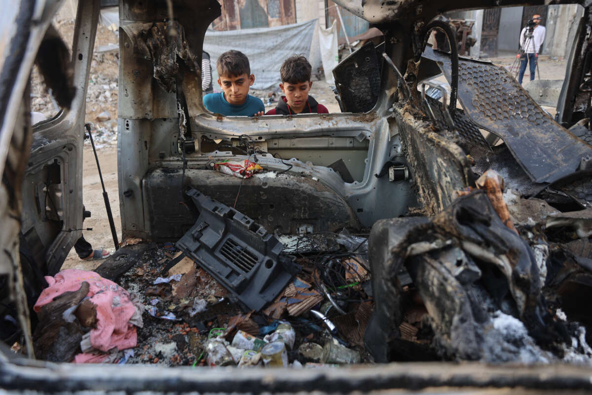Palestinian displaced children look at a destroyed vehicle targeted by the Israeli military, in Gaza City, on November 22, 2025.