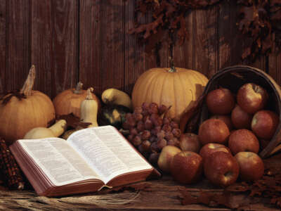 A whitewashed version of Thanksgiving is portrayed with an open Bible, a basket of apples, and pumpkins.
