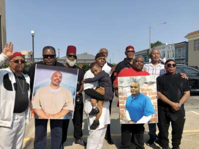 Holding images of John "Balagoon" Cole (left) and Christopher "Naeem" Trotter (right), known as “the Pendleton 2,” men who've been incarcerated with them over the past 40 years rally for their release.
